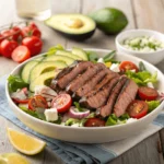 Grilled steak slices on a bed of fresh mixed greens with cherry tomatoes and avocado