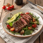 Grilled ribeye steak served on a fresh mixed greens salad with cherry tomatoes and avocado slices